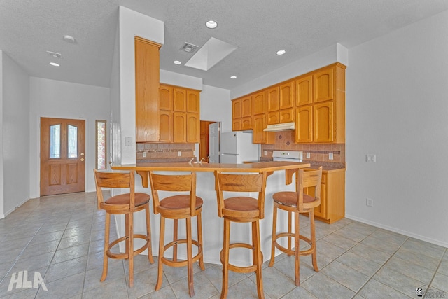 kitchen with decorative backsplash, a skylight, freestanding refrigerator, a peninsula, and under cabinet range hood