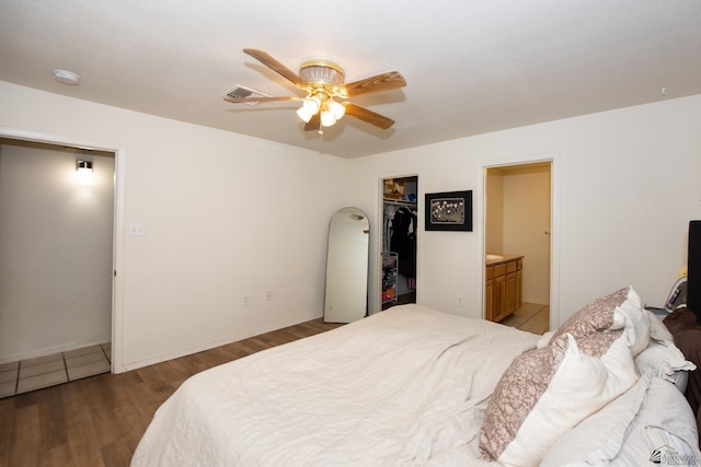 bedroom with connected bathroom, wood finished floors, a spacious closet, visible vents, and a closet