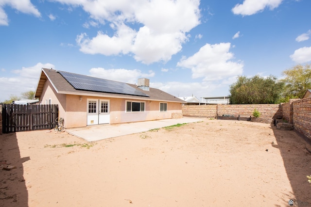rear view of property with a shingled roof, stucco siding, a fenced backyard, solar panels, and a patio