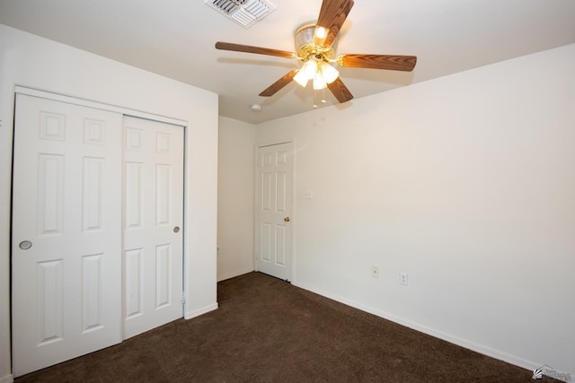 unfurnished bedroom with visible vents, a closet, baseboards, dark colored carpet, and ceiling fan