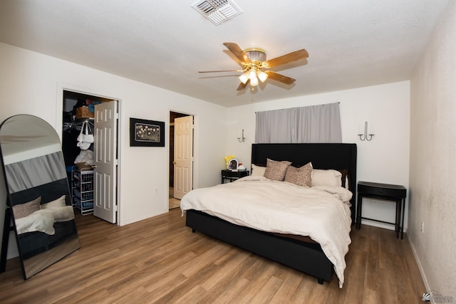 bedroom featuring visible vents, a closet, wood finished floors, a walk in closet, and ceiling fan