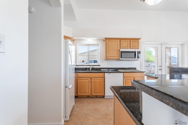 kitchen featuring a sink, dark stone countertops, light brown cabinetry, and white appliances