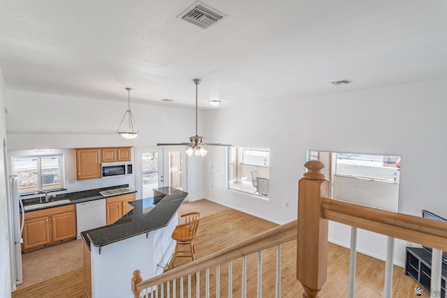 kitchen with a kitchen island, a kitchen bar, visible vents, light wood-type flooring, and white appliances