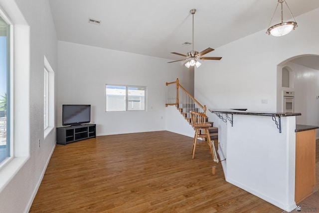 unfurnished living room with ceiling fan, visible vents, arched walkways, wood finished floors, and stairway