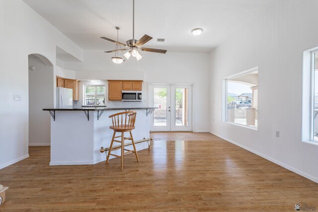 kitchen featuring ceiling fan, a kitchen breakfast bar, stainless steel microwave, freestanding refrigerator, and light wood finished floors