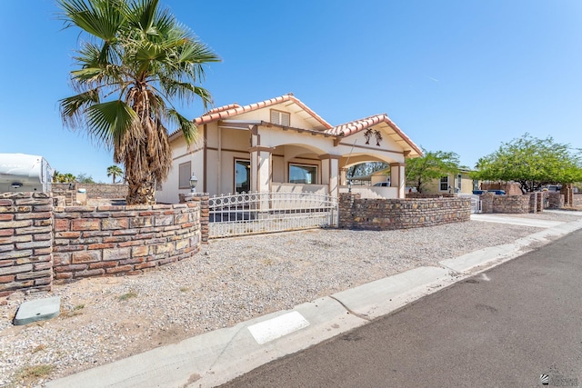 mediterranean / spanish home with a tiled roof, a fenced front yard, a gate, and stucco siding