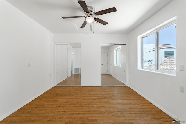 unfurnished bedroom with visible vents, two closets, baseboards, ceiling fan, and light wood-style flooring