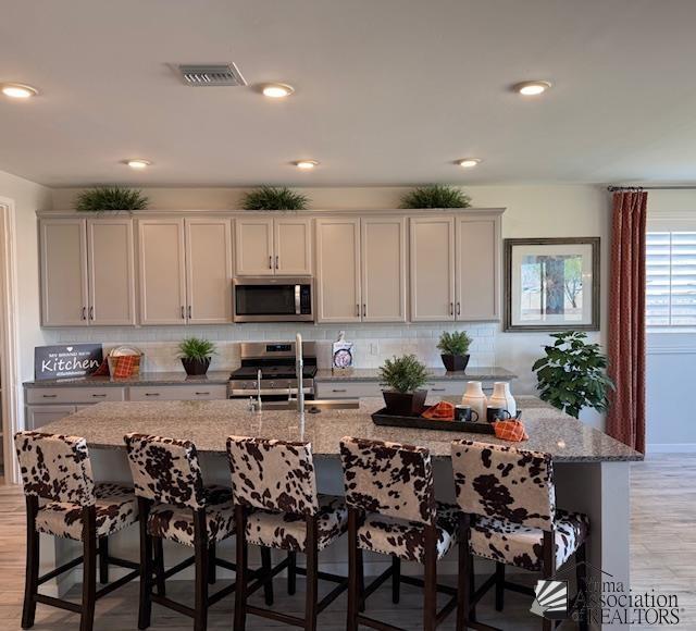 14700 E 42nd Pl, Yuma, AZ 85367 - kitchen with stainless steel appliances, tasteful backsplash, light stone countertops, a kitchen bar, and light wood finished floors