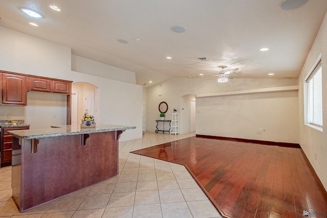11594 E 27th Pl, Yuma, AZ 85367 - kitchen with arched walkways, vaulted ceiling, a breakfast bar area, a ceiling fan, and light stone counters