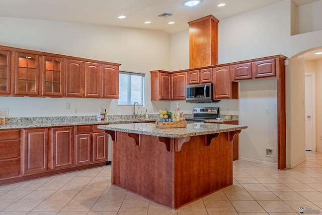 11594 E 27th Pl, Yuma, AZ 85367 - kitchen with stainless steel appliances, a high ceiling, light tile patterned floors, light stone counters, and glass insert cabinets