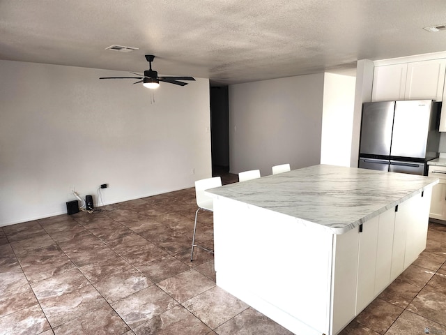 kitchen with visible vents, freestanding refrigerator, a center island, a textured ceiling, and a ceiling fan