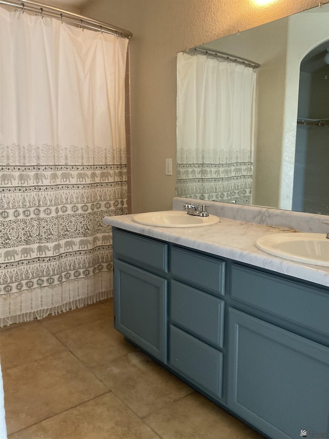 bathroom featuring a shower with shower curtain, double vanity, tile patterned floors, and a sink