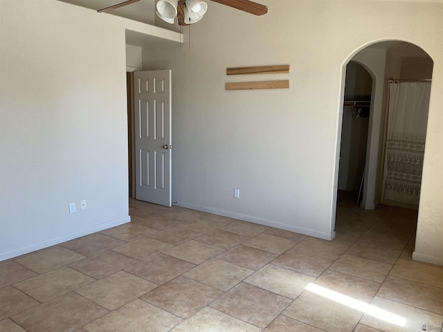 unfurnished bedroom featuring ceiling fan, a walk in closet, arched walkways, baseboards, and a closet