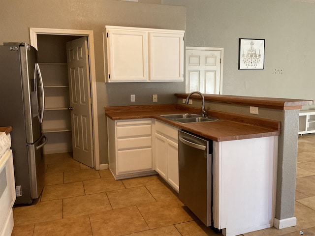 kitchen with a peninsula, light tile patterned flooring, white cabinetry, a sink, and appliances with stainless steel finishes