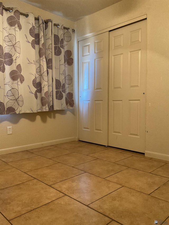 unfurnished bedroom featuring light tile patterned flooring, baseboards, and a closet