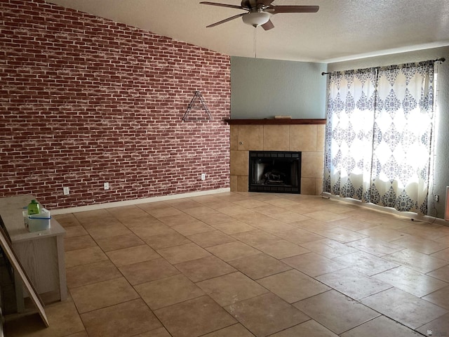 unfurnished living room with brick wall, a textured ceiling, a ceiling fan, a tile fireplace, and vaulted ceiling