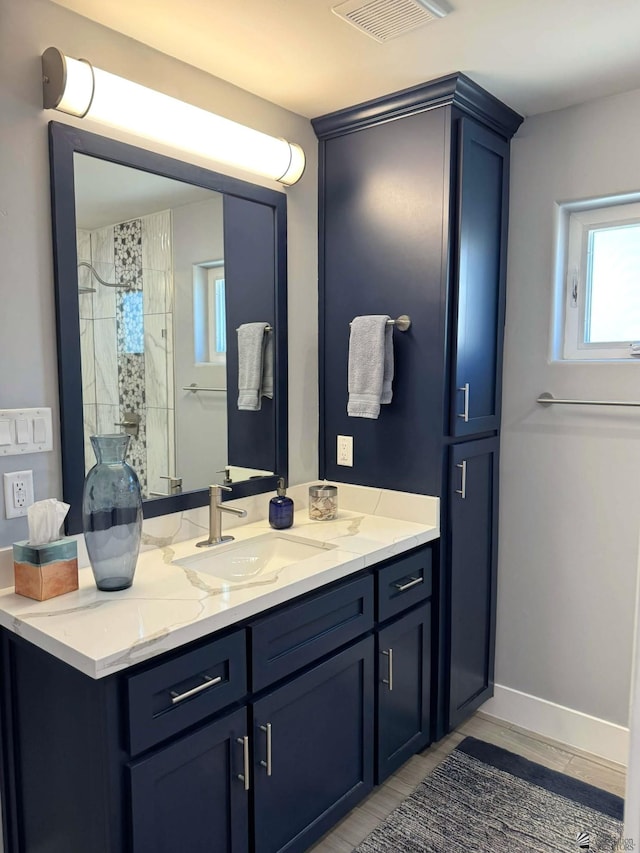 bathroom with visible vents, baseboards, tiled shower, and vanity