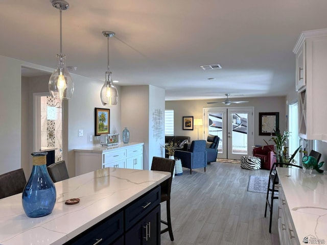 kitchen featuring visible vents, open floor plan, white cabinets, light stone counters, and light wood finished floors