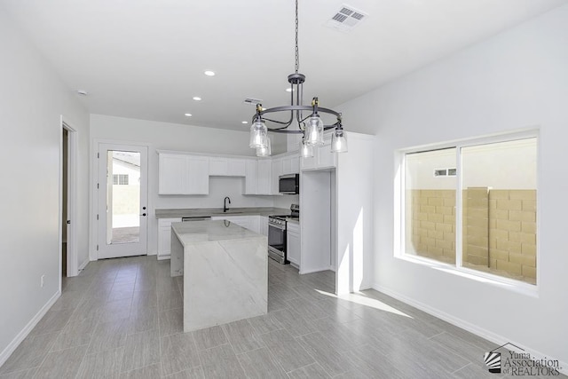 kitchen with a center island, white cabinetry, a sink, appliances with stainless steel finishes, and a notable chandelier