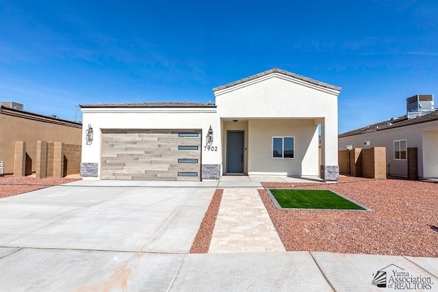 view of front facade with central AC, stone siding, a garage, stucco siding, and concrete driveway