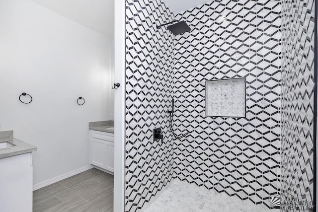 full bathroom with vanity, baseboards, and a tile shower