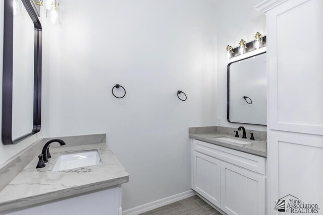 full bathroom with a sink, baseboards, and two vanities