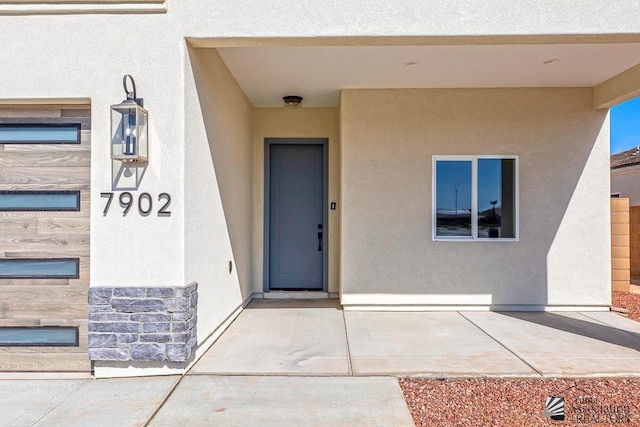 doorway to property featuring stucco siding, a patio area, and stone siding