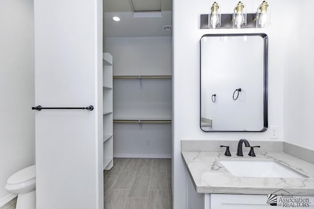 bathroom with a walk in closet, vanity, toilet, recessed lighting, and baseboards