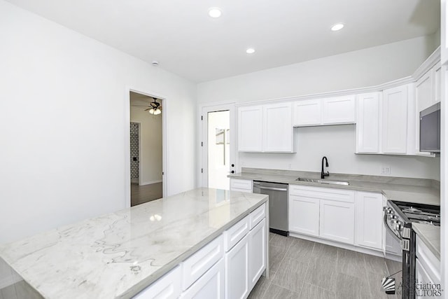 kitchen with white cabinets, stainless steel appliances, light stone countertops, and a sink