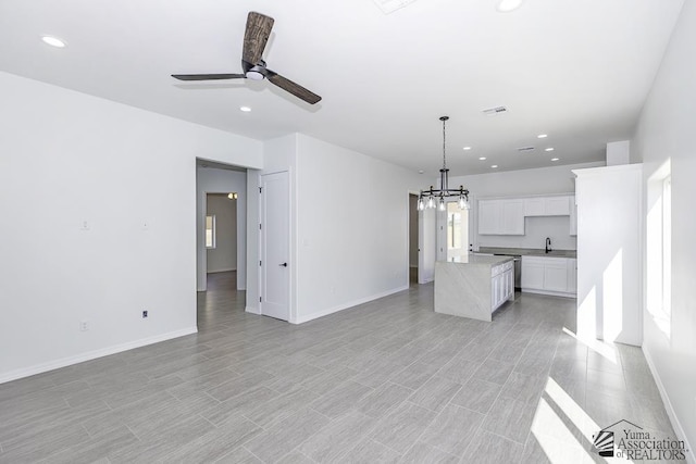 unfurnished living room with recessed lighting, a sink, baseboards, and ceiling fan with notable chandelier