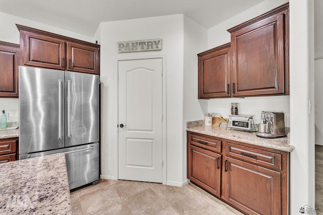 kitchen with high end refrigerator, light stone counters, and light tile patterned floors