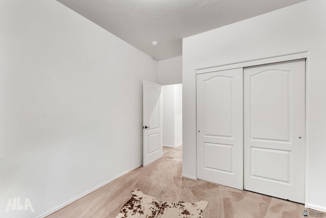 unfurnished bedroom with light colored carpet, a textured ceiling, and a closet