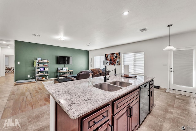 kitchen featuring sink, hanging light fixtures, dishwasher, an island with sink, and light stone countertops