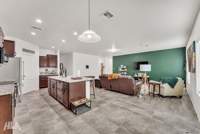 kitchen featuring sink, dark brown cabinets, light stone counters, a center island with sink, and decorative light fixtures