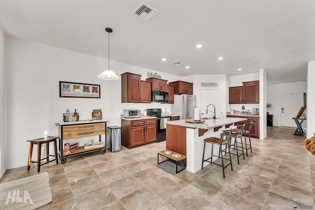 kitchen featuring sink, a breakfast bar, hanging light fixtures, black appliances, and a center island with sink