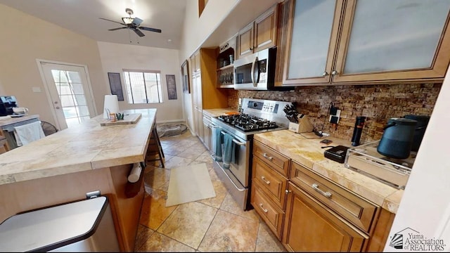 kitchen with light tile patterned flooring, brown cabinetry, stainless steel appliances, a ceiling fan, and backsplash
