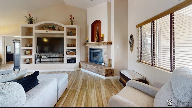 living room with light wood-type flooring, a high end fireplace, baseboards, and vaulted ceiling