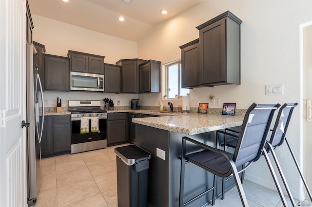11602 E 33rd St, Yuma, AZ 85367 - kitchen featuring a peninsula, light tile patterned flooring, light stone countertops, a kitchen bar, and appliances with stainless steel finishes
