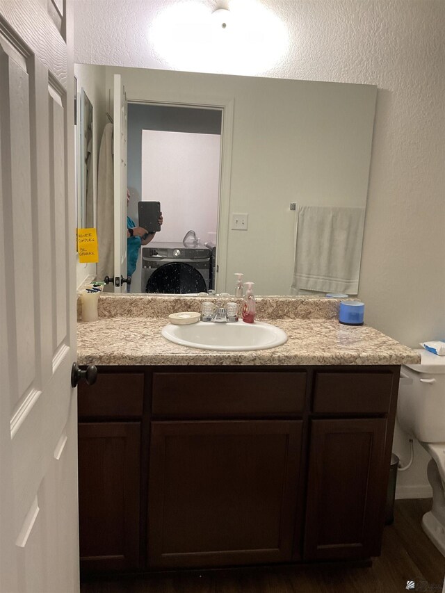 bathroom featuring vanity, washer / dryer, wood finished floors, and toilet