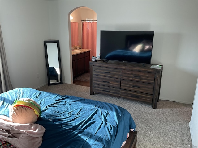 carpeted bedroom with baseboards, arched walkways, a sink, and ensuite bathroom