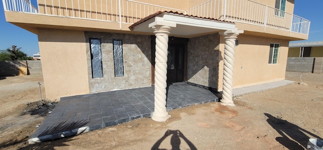 view of exterior entry with stucco siding, a balcony, and fence