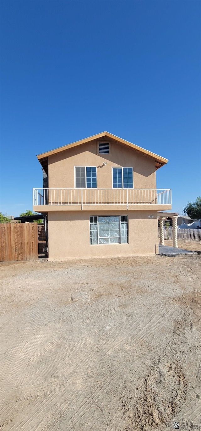 view of side of property featuring fence, stucco siding, and a balcony