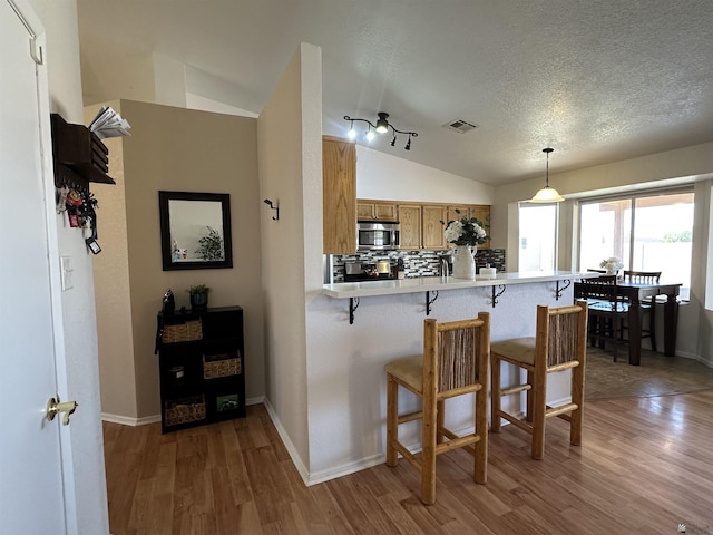 11228 E 25th St, Yuma, AZ 85367 - kitchen with stainless steel microwave, lofted ceiling, brown cabinetry, a kitchen breakfast bar, and a textured ceiling