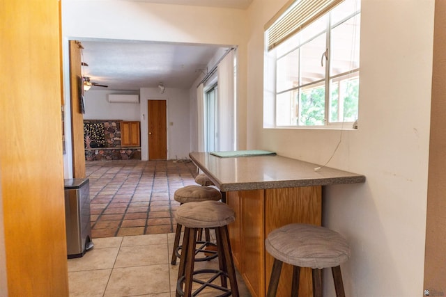 bar featuring light tile patterned floors, ceiling fan, a bar, and an AC wall unit