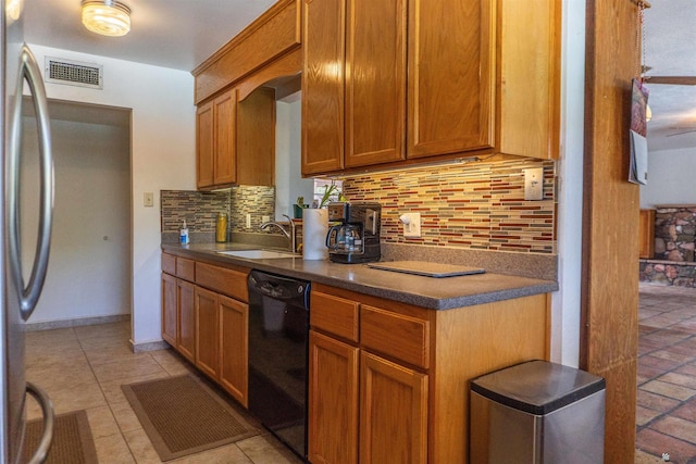 kitchen featuring dark countertops, stainless steel fridge, a sink, black dishwasher, and decorative backsplash