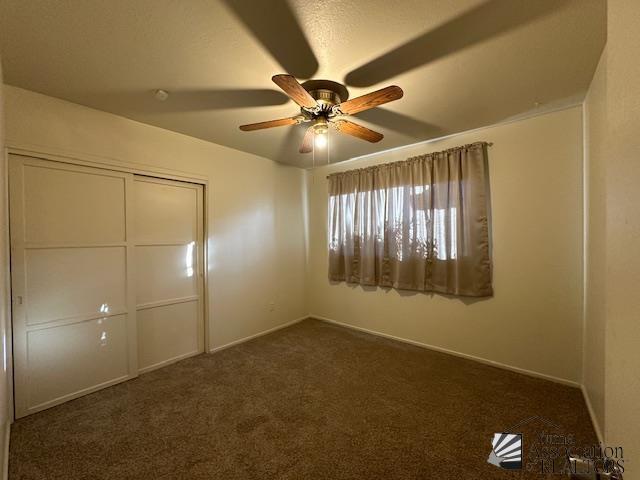 unfurnished bedroom featuring baseboards, ceiling fan, a closet, and dark colored carpet