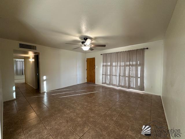 unfurnished room featuring visible vents, dark tile patterned floors, and ceiling fan