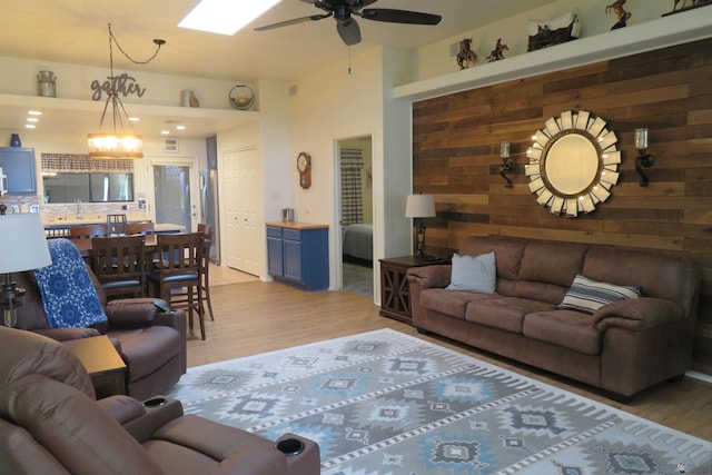 living room with sink, ceiling fan with notable chandelier, light hardwood / wood-style flooring, and wood walls