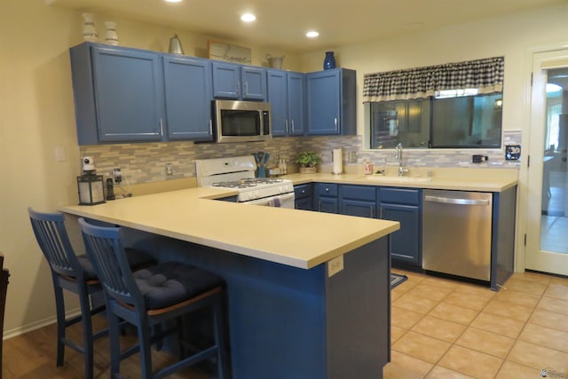 kitchen featuring blue cabinets, sink, appliances with stainless steel finishes, kitchen peninsula, and a breakfast bar area