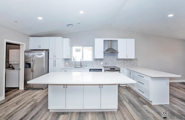 kitchen with sink, a kitchen island, stainless steel appliances, stacked washing maching and dryer, and wall chimney range hood